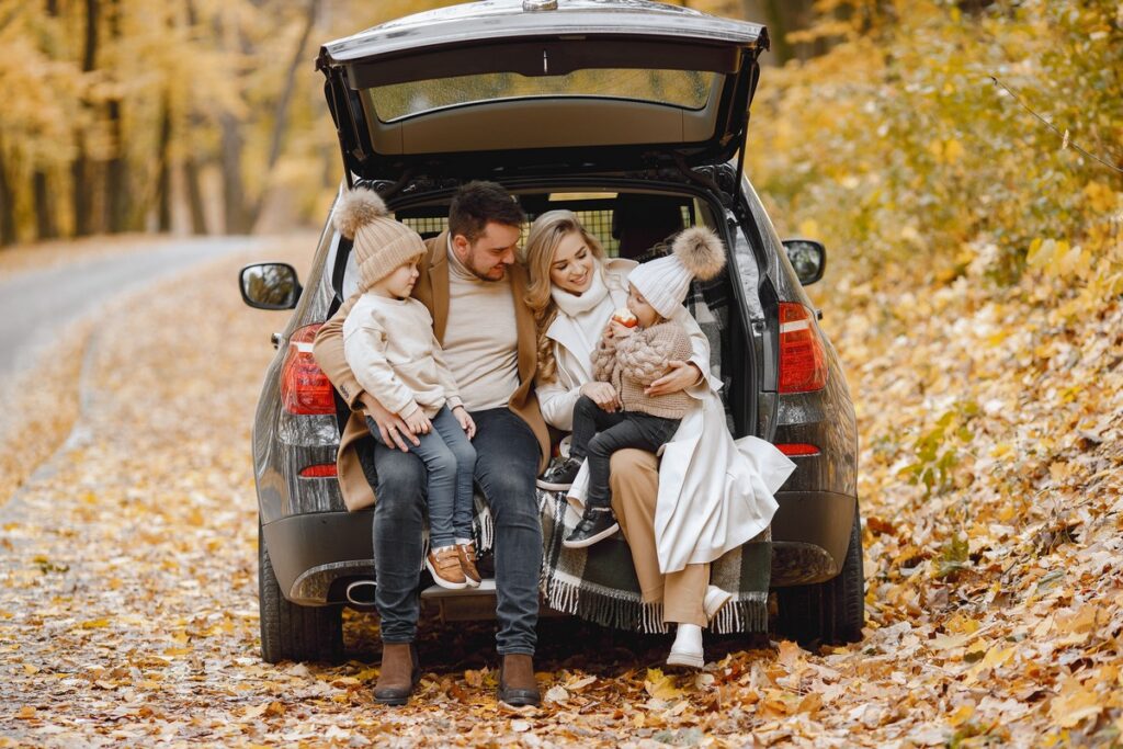 happy family resting after day spending outdoor autumn park father mother two children sitting inside car trunk smiling family holiday traveling concept