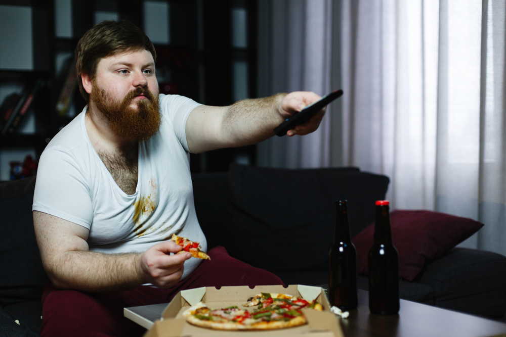 fat man eats pizza sitting sofa switches channels tv set