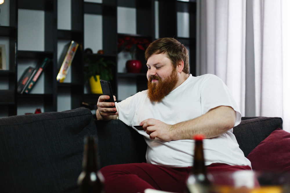 fat man types number credit card his phone sitting couch 1