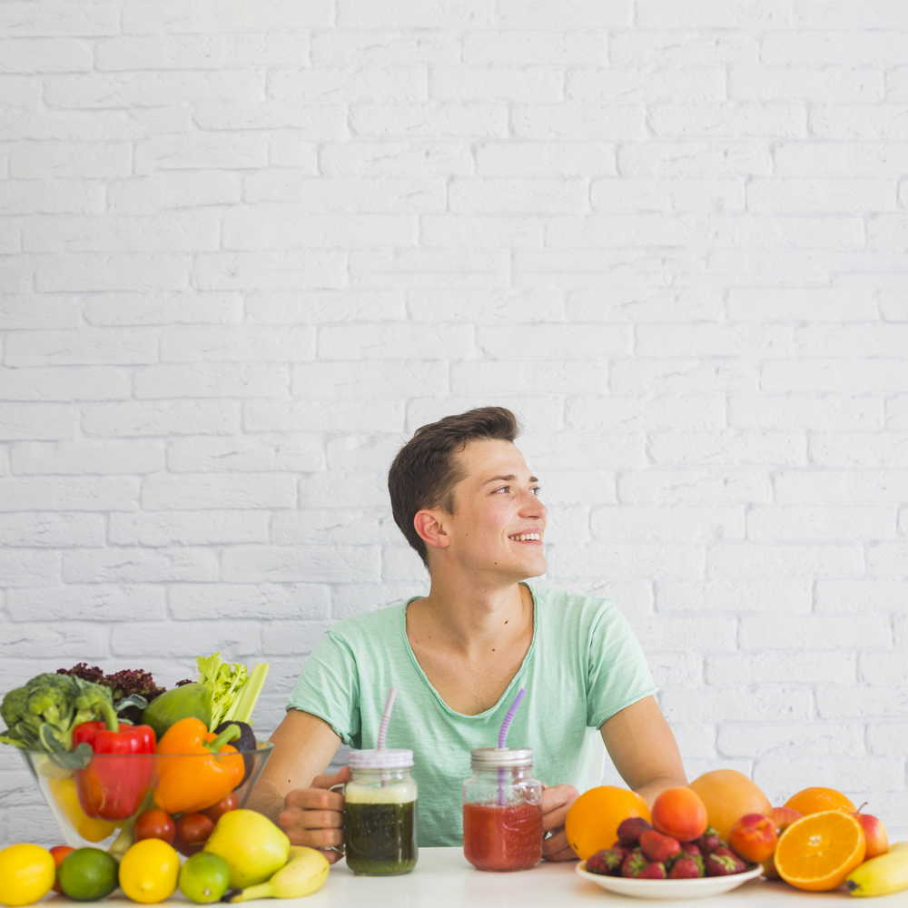 smiling young man sitting table with ripe fresh vegetables fruits