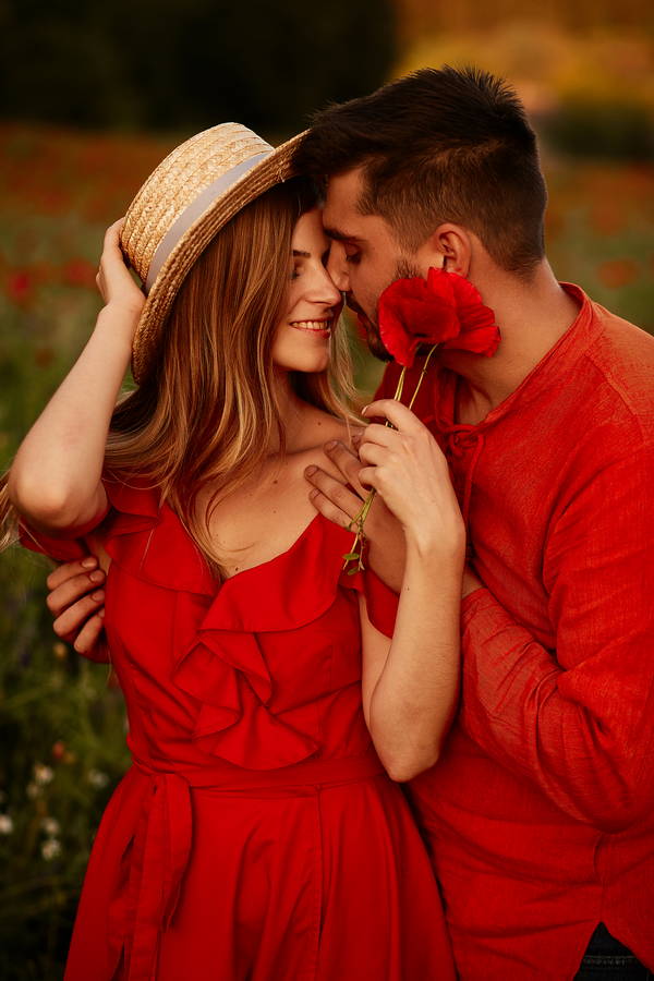 man holds tender beautiful woman standing with her green field with red poppies